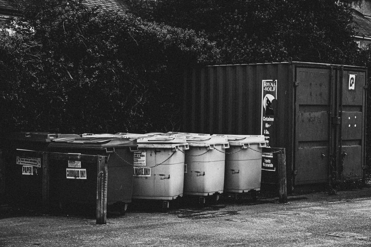 A row of large wheeled waste bins beside a storage container