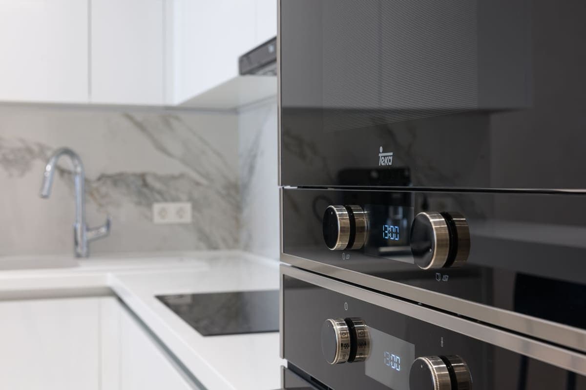 A white kitchen with a marble splashback and a built-in oven