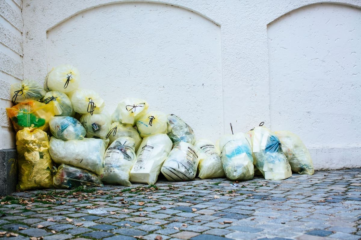 Filled translucent plastic trash bags stacked against a wall