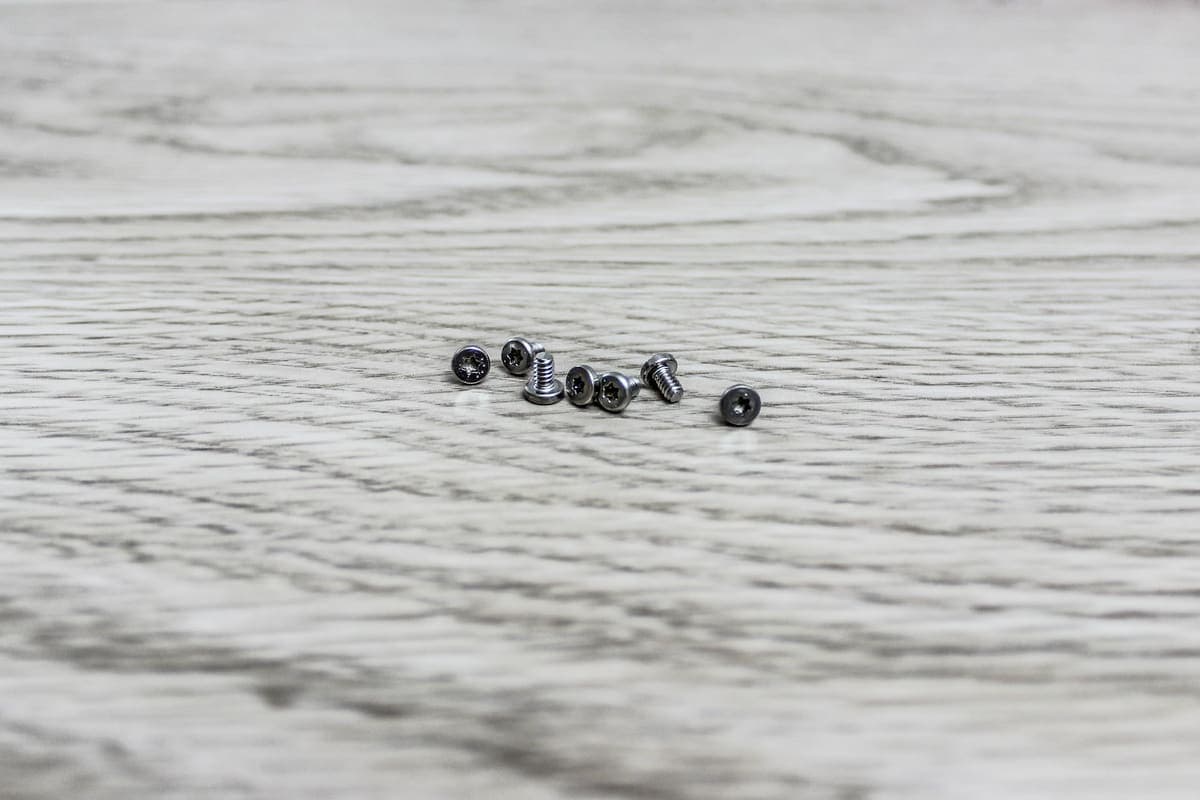 Small silver screws scattered on a pale wood surface