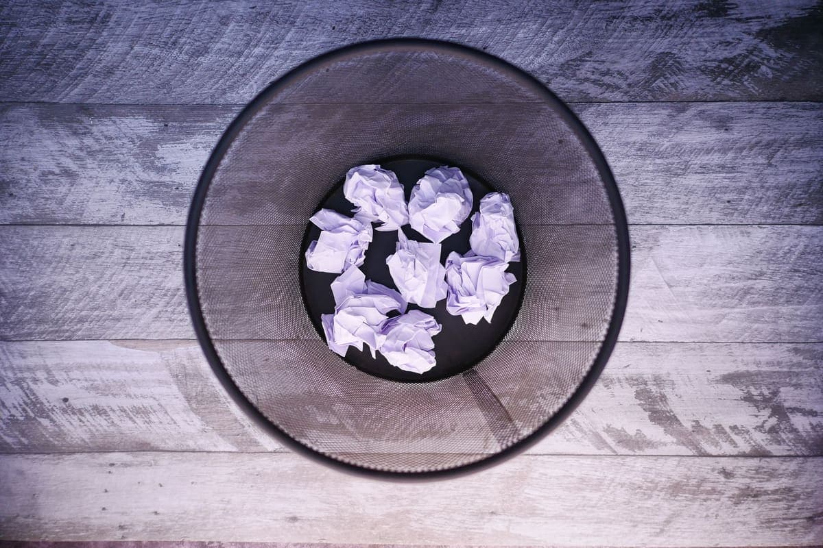 An open mesh wastepaper basket seen from above, with crumpled paper inside