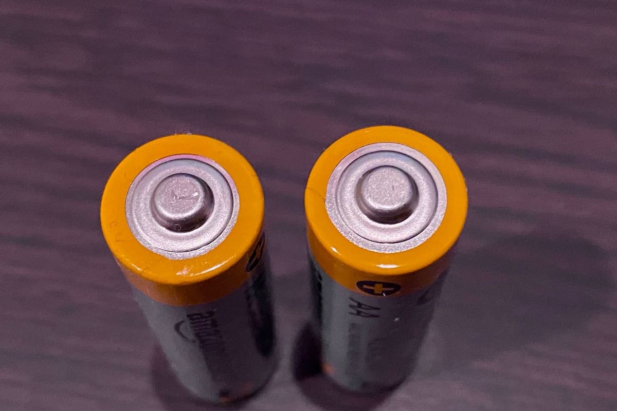 Two alkaline batteries standing on a dark surface