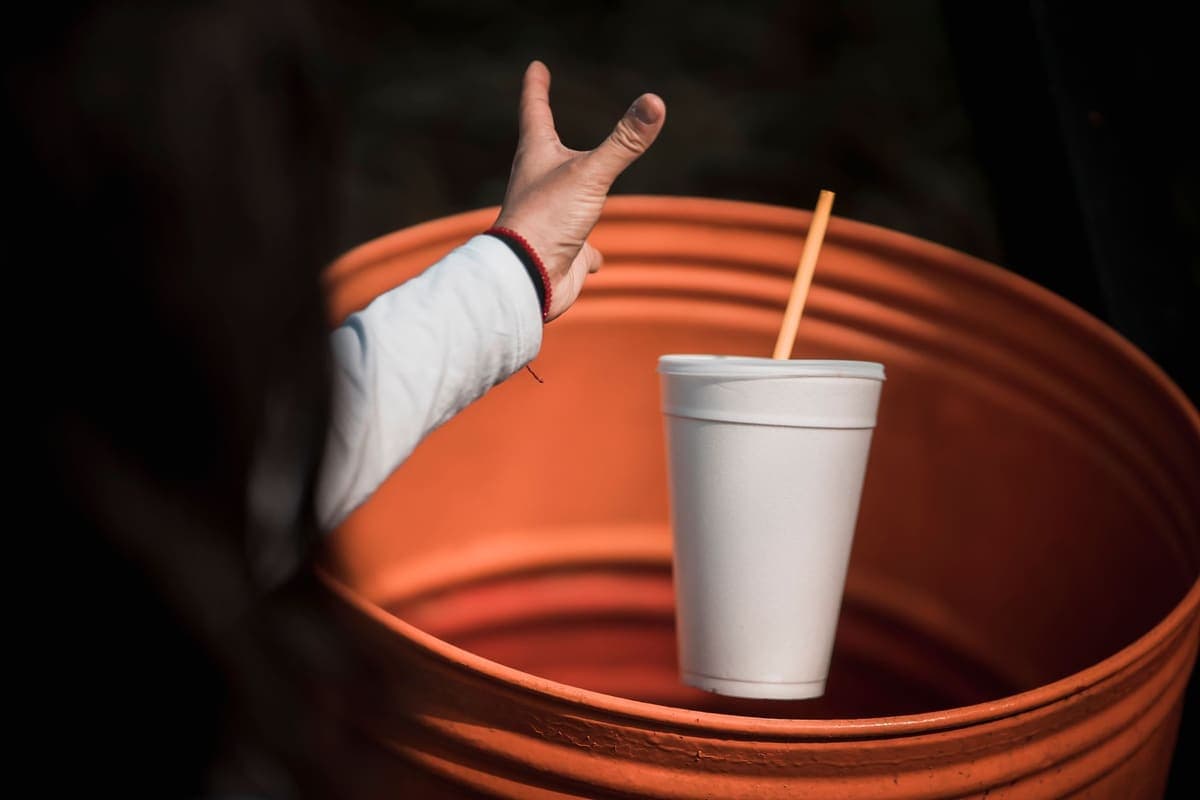 Hand dropping a cup into an orange trash can
